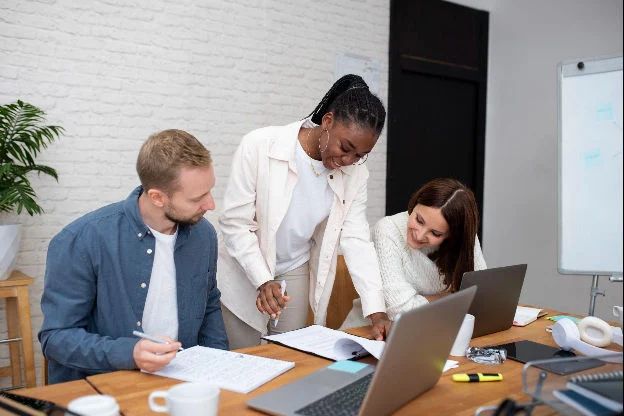 Three colleagues review documents at a desk; one points to a page.