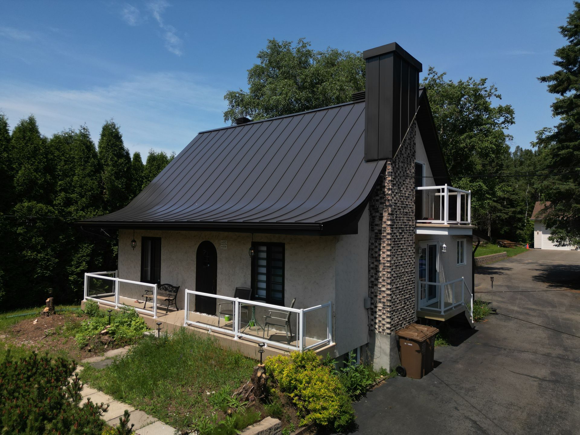 Maison avec toit et cheminée en métal noir, murs en stuc blanc et balcon.