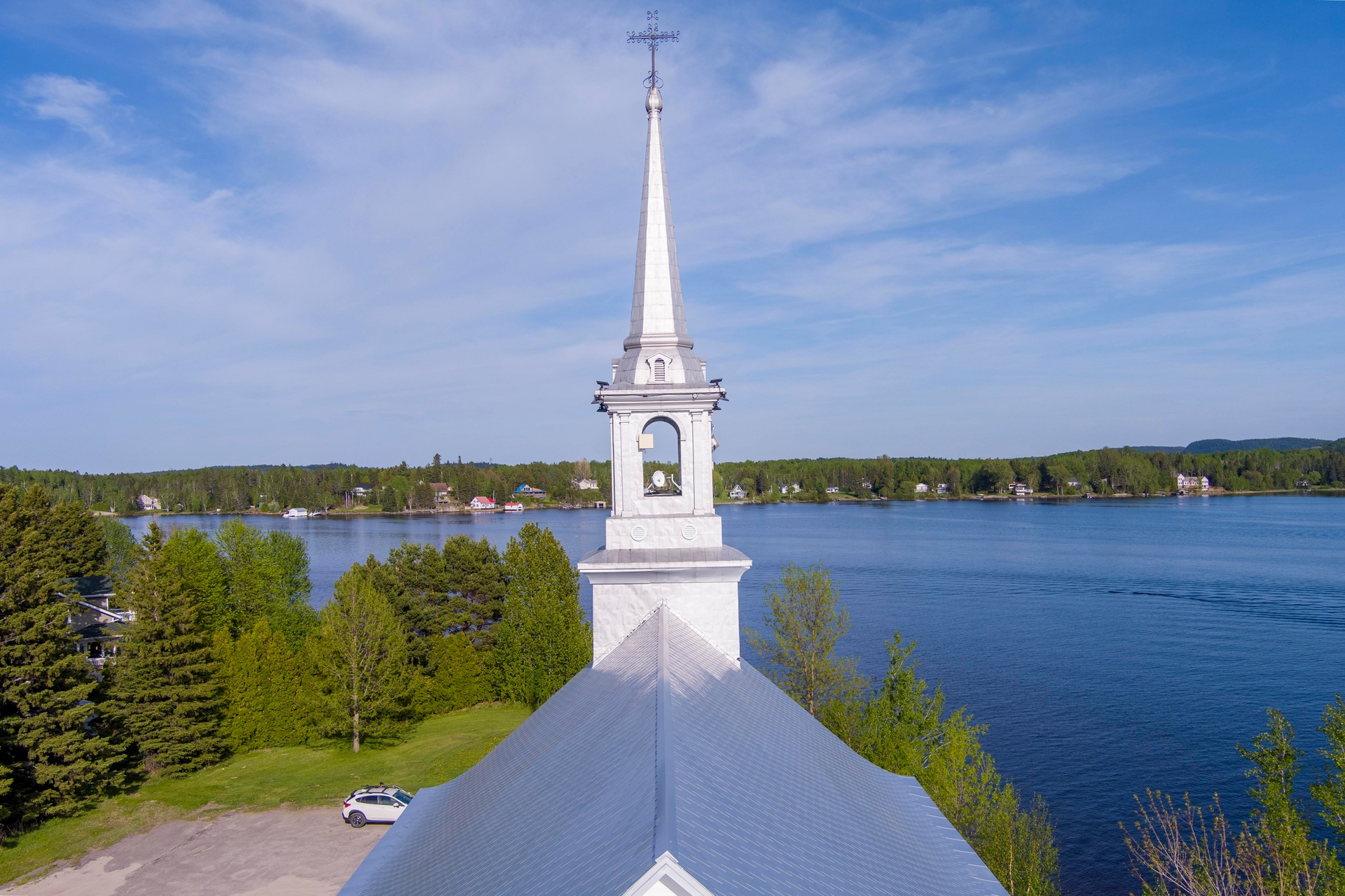 Clocher blanc d'une église se détachant sur un ciel bleu, surplombant un lac.