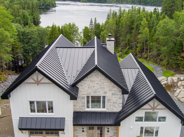 Maison avec toit en métal noir et façade en pierre, donnant sur un lac et une forêt.