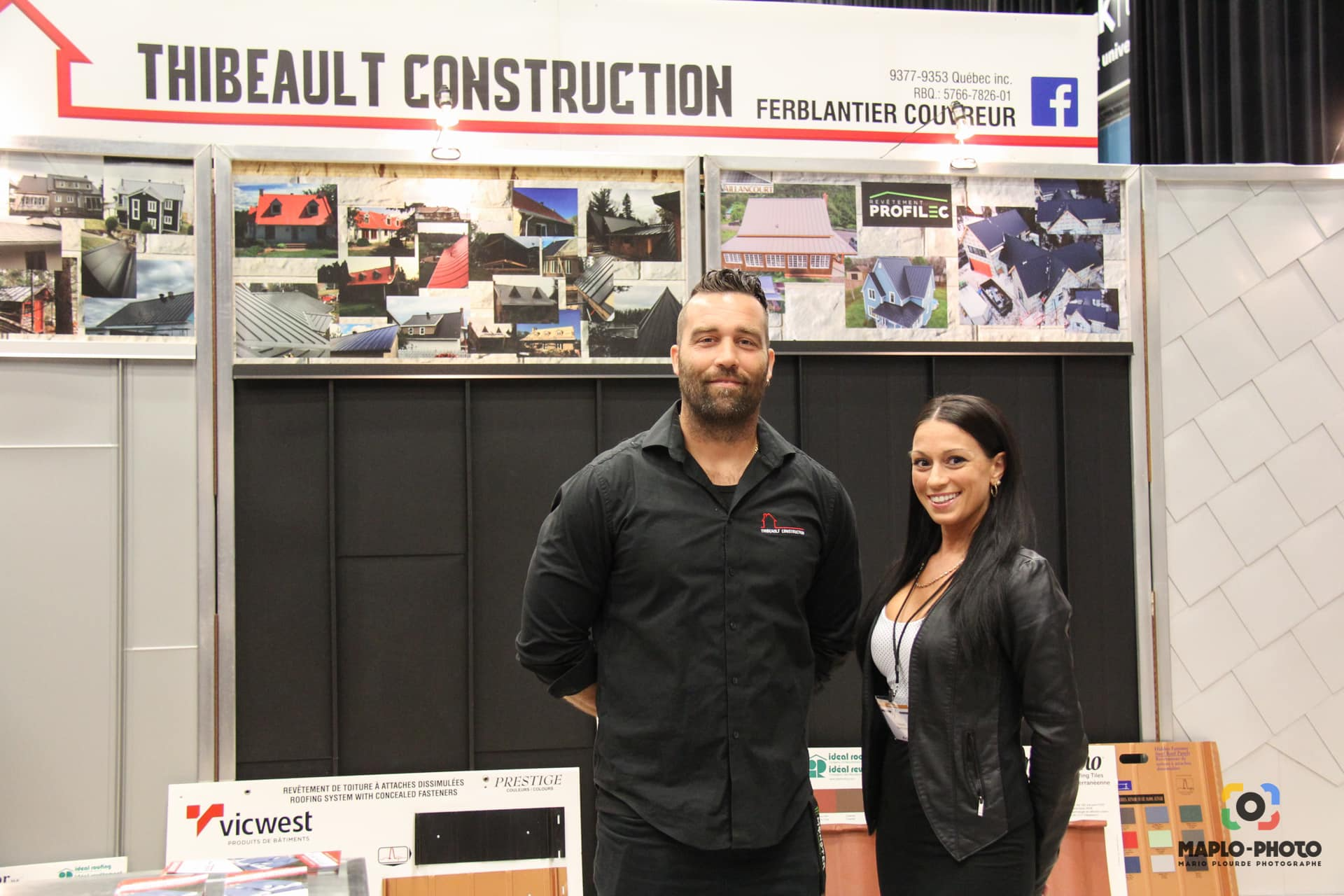Deux personnes sur le stand de Thibeault Construction lors d'un salon professionnel. Un homme en chemise noire, une femme en veste noire. Des photos de projets sont exposées.