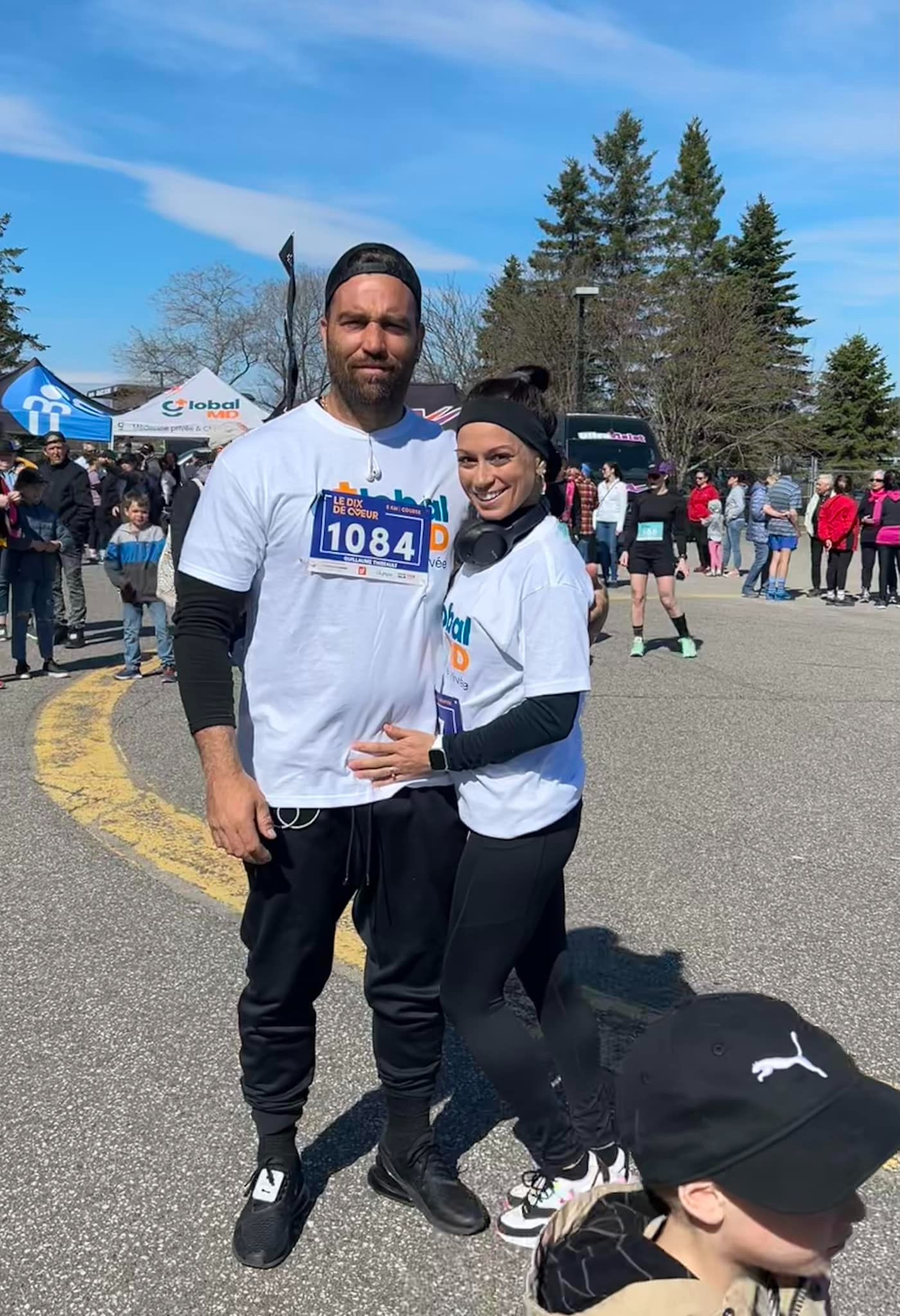 Un couple pose lors d'un événement en plein air, portant des t-shirts assortis avec le logo de l'événement, par une journée ensoleillée.