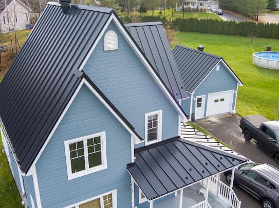 Maison bleue avec toit en métal noir, boiseries blanches et une voiture dans l'allée.