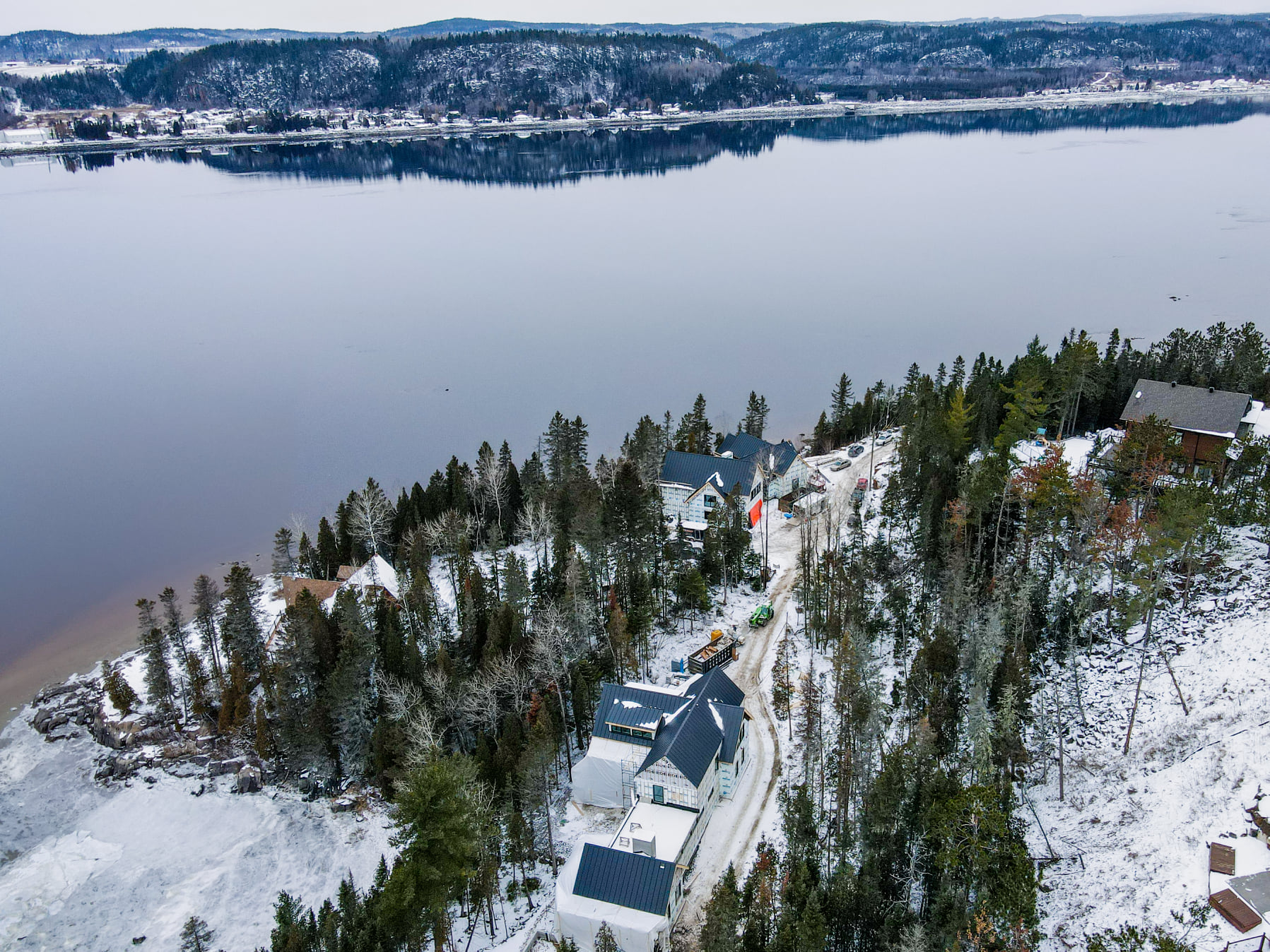 Paysage enneigé au bord de l'eau, avec des maisons nichées parmi les arbres et un lac en arrière-plan.