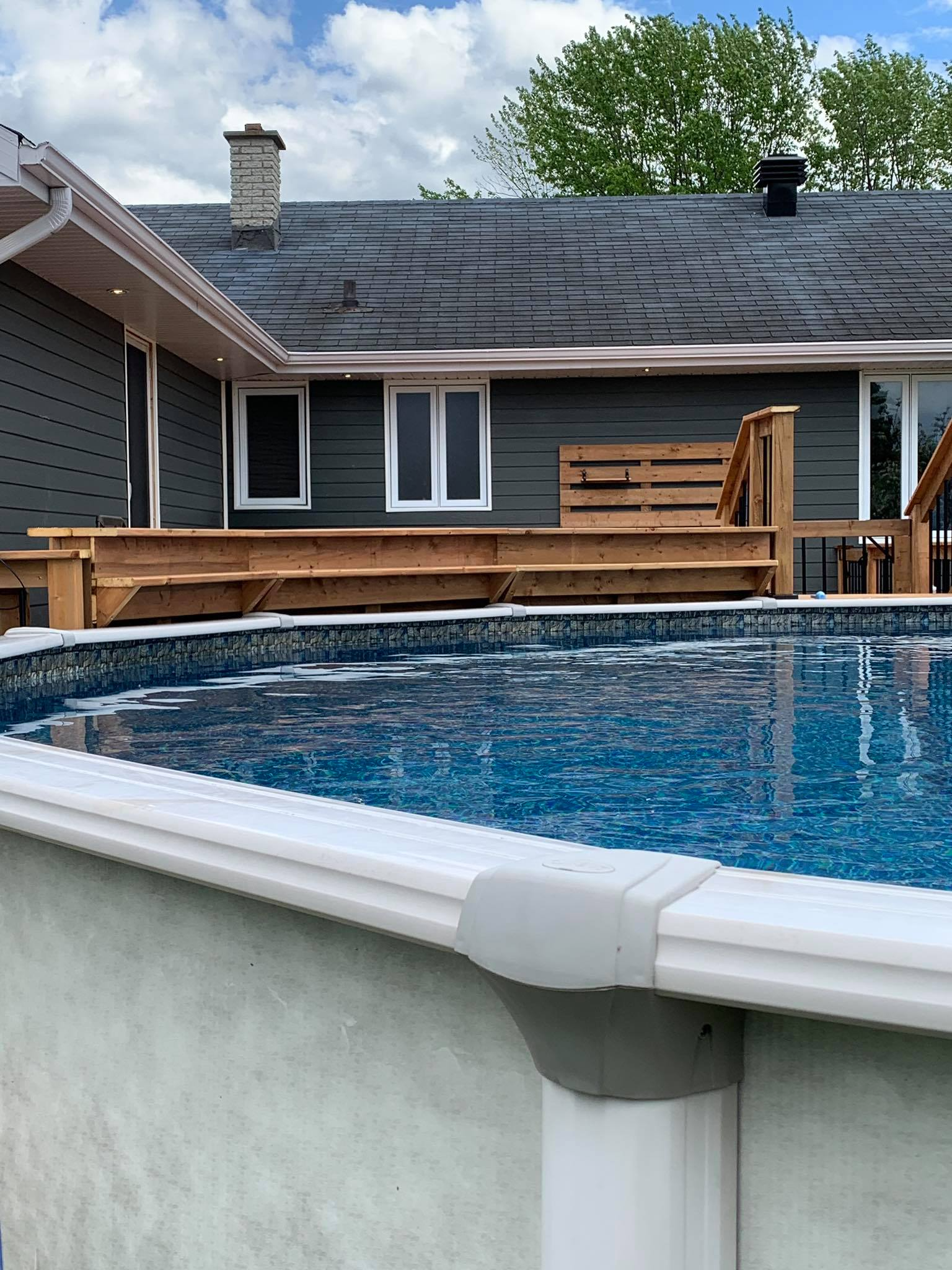 Piscine hors sol avec terrasse et maison en arrière-plan par temps nuageux.