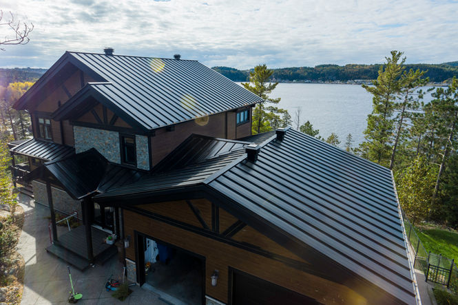 Maison à deux étages avec toit en métal noir et éléments en bois, donnant sur un lac.