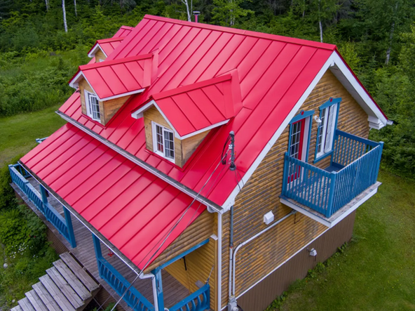 Maison avec un toit en métal rouge vif, un porche et un balcon bleus. Située dans un quartier boisé et verdoyant.
