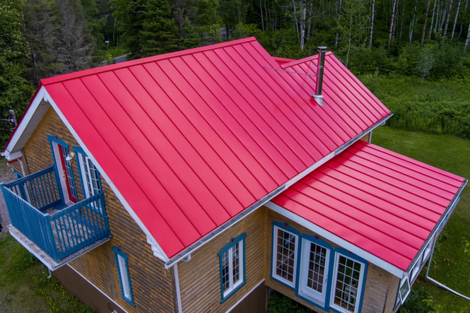 Toit en métal rouge sur une maison beige avec des touches de bleu et des finitions blanches, entourée d'arbres verts.