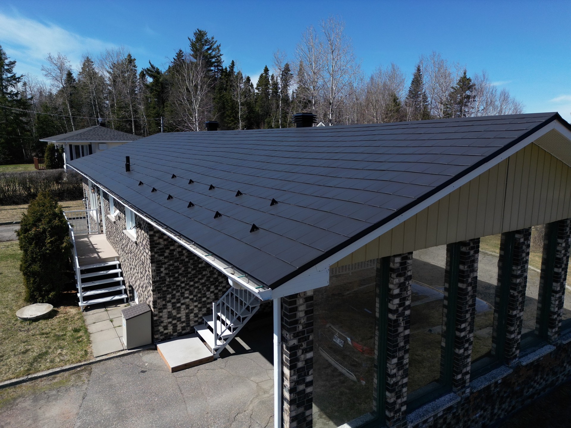 Une maison avec un toit en métal noir, des piliers en pierre et un escalier, par une journée ensoleillée.