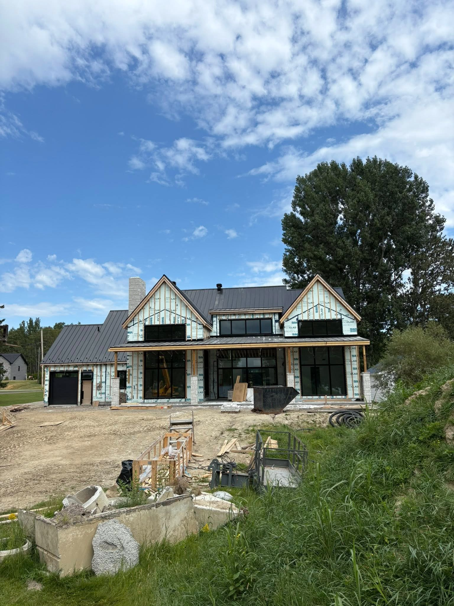 Maison en construction par une journée ensoleillée, sous un ciel bleu, avec un toit partiellement construit.