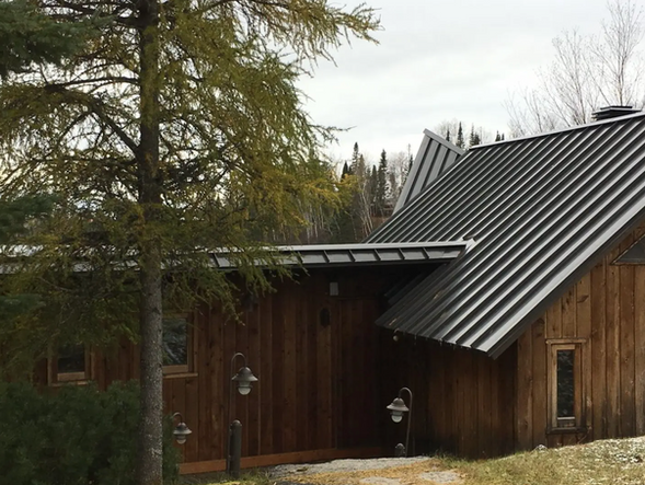 Bâtiment en bois avec toit en métal ; arbre au premier plan, ciel nuageux.