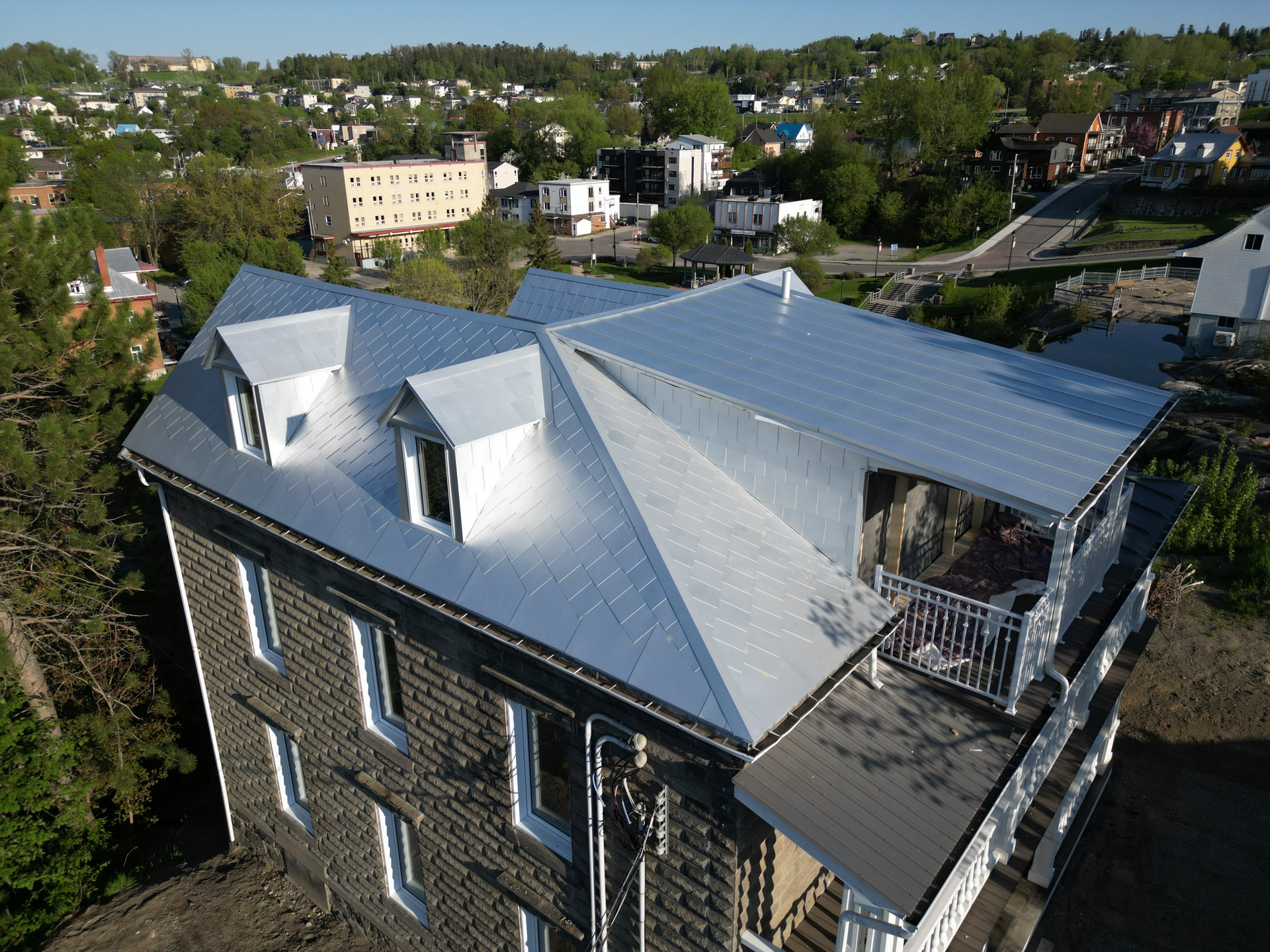 Vue aérienne d'un immeuble à plusieurs étages avec un toit en métal argenté, des lucarnes et un petit balcon.