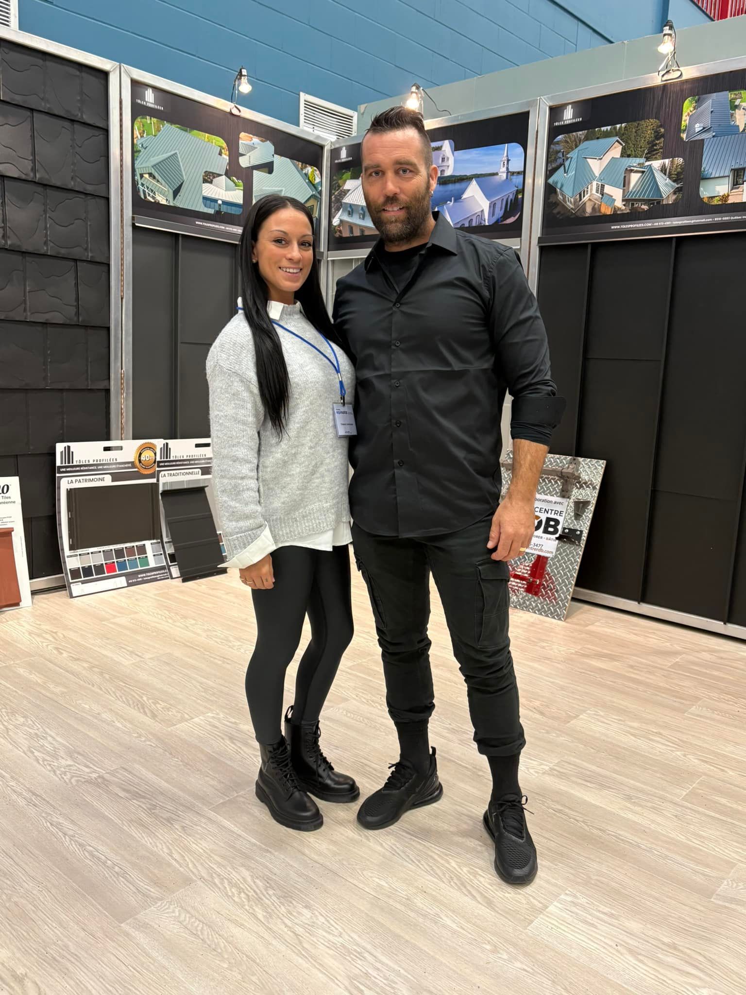 Deux personnes se tiennent côte à côte devant un stand d'exposition. Elles portent des vêtements noirs décontractés.