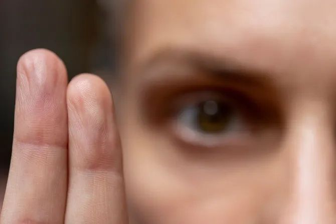 A close-up of two fingers held upright in front of a slightly blurred human eye.