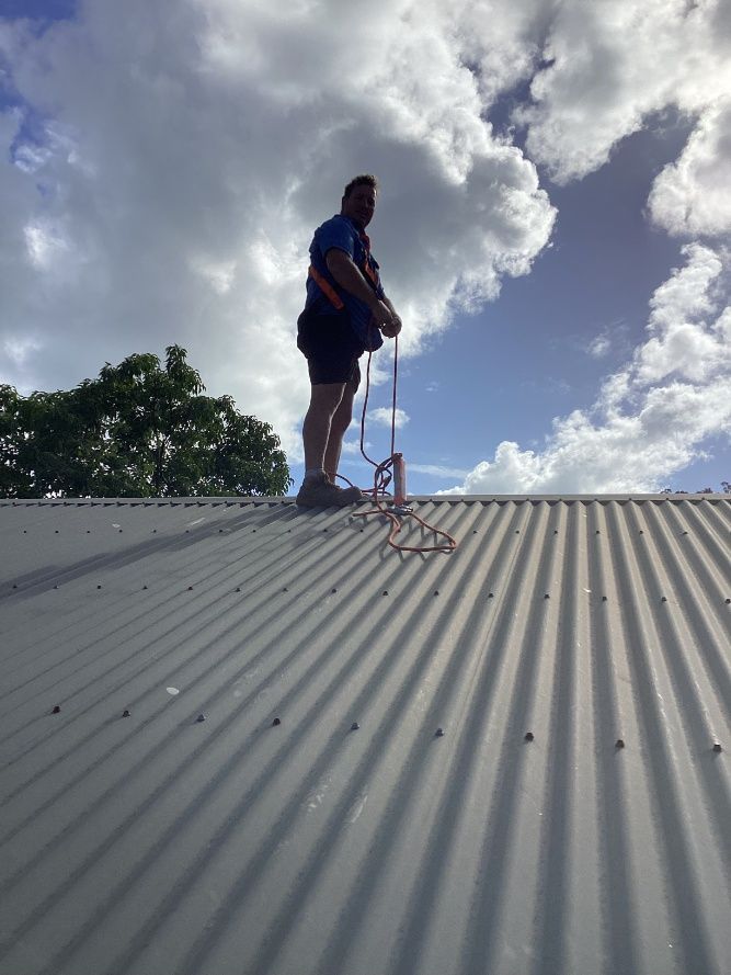 A Man is Standing on Top of a Corrugated Metal Roof — Pain in the Glass Window Cleaning in Cannonvale, QLD