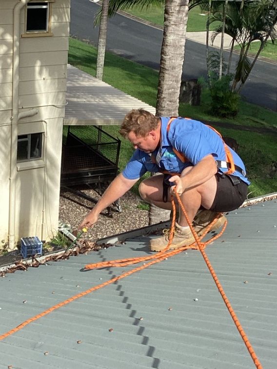 A Man is Kneeling on a Roof With a Rope Around His Waist — Pain in the Glass Window Cleaning in Cannonvale, QLD