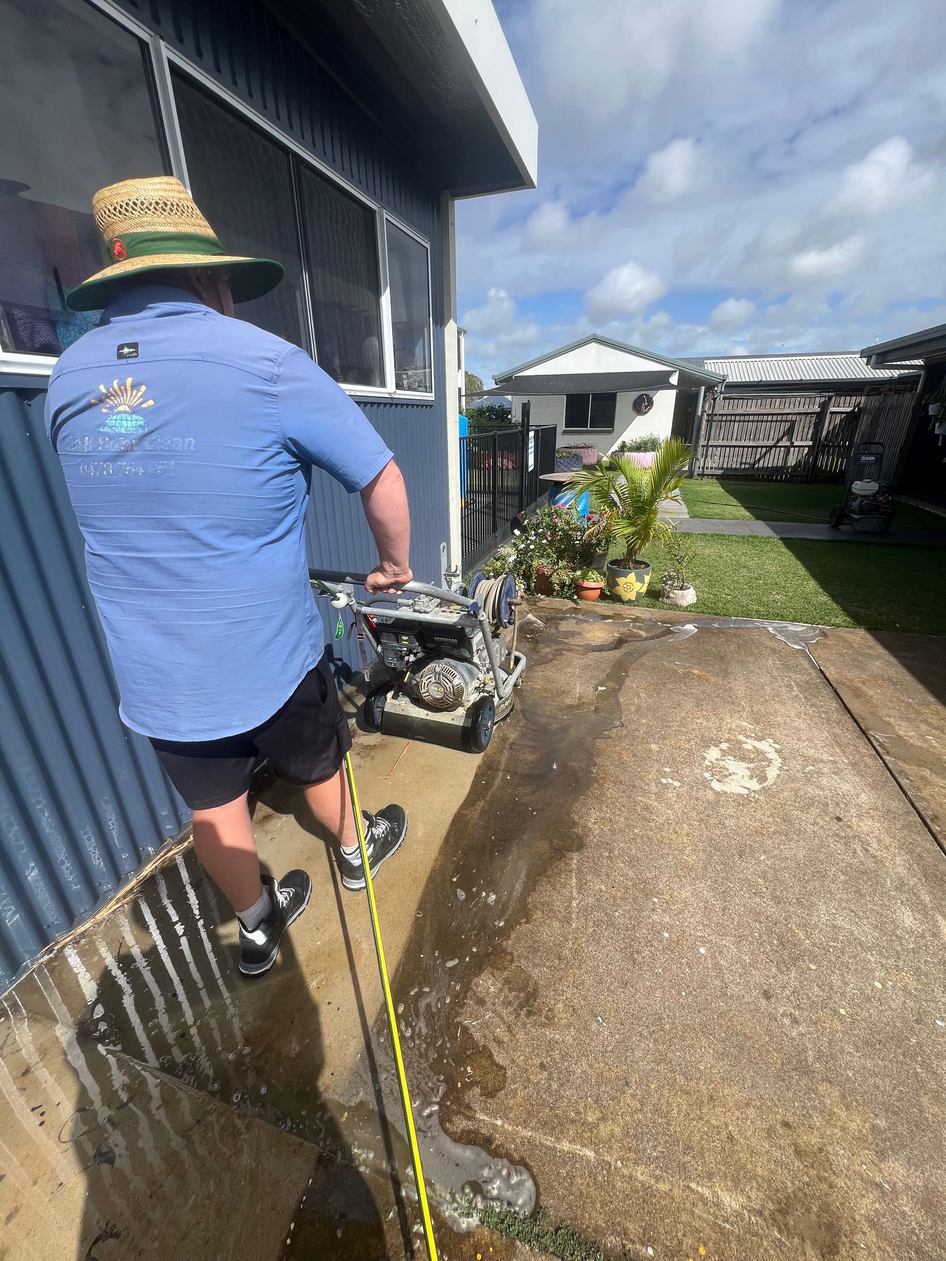 A person is using a high pressure washer to clean a concrete floor — Pain in the Glass Window Cleaning in Cannonvale, QLD
