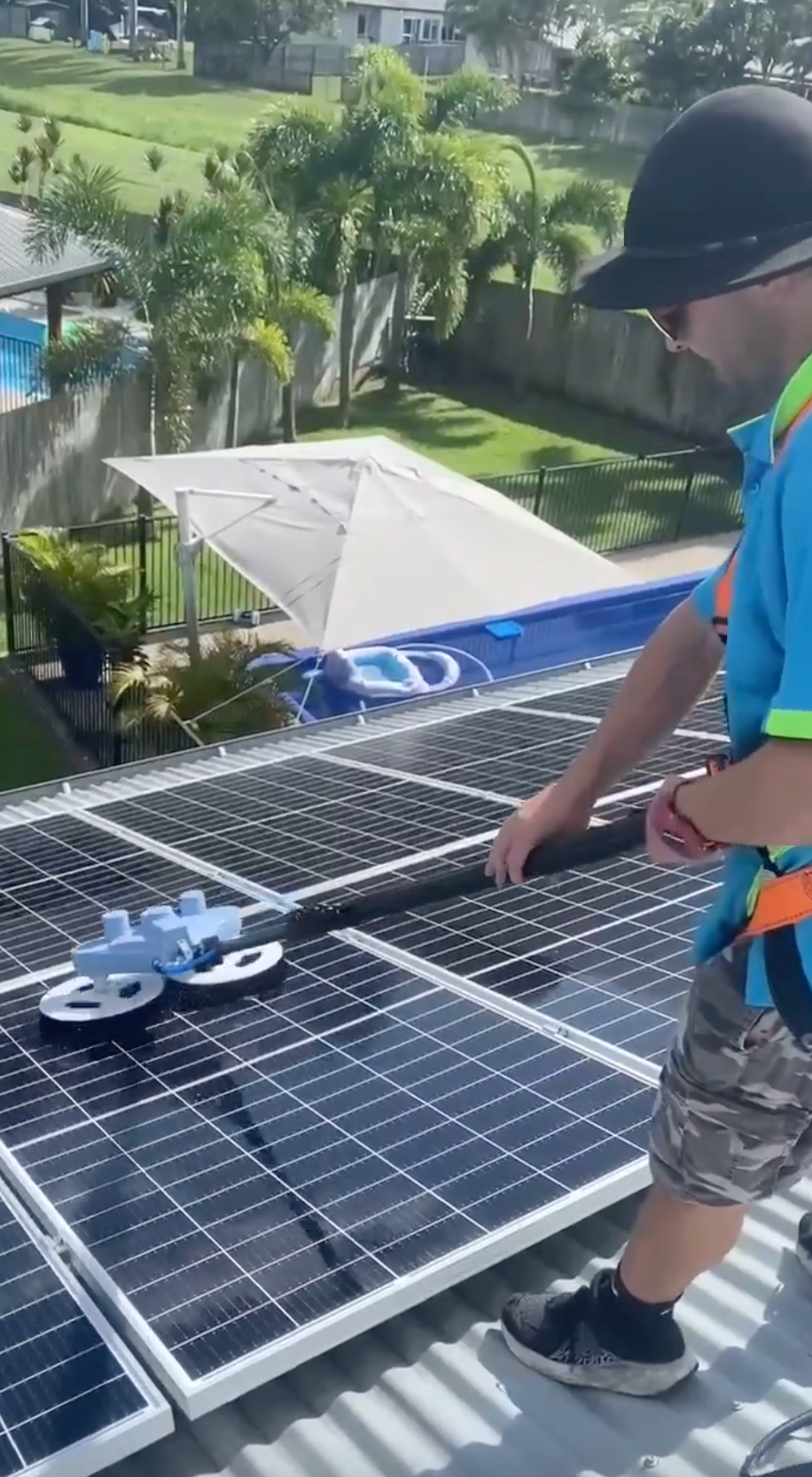 A Man is Cleaning Solar Panels With a Broom — Pain in the Glass Window Cleaning in Cannonvale, QLD