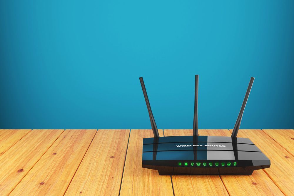 A Router Is Sitting On A Wooden Table In Front Of A Blue Wall — Comms Cabling Central Coast In Kanwal, NSW