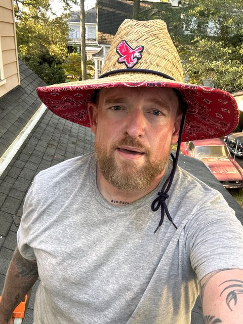 Person connecting black drainage pipe to a gutter spout in a yard.
