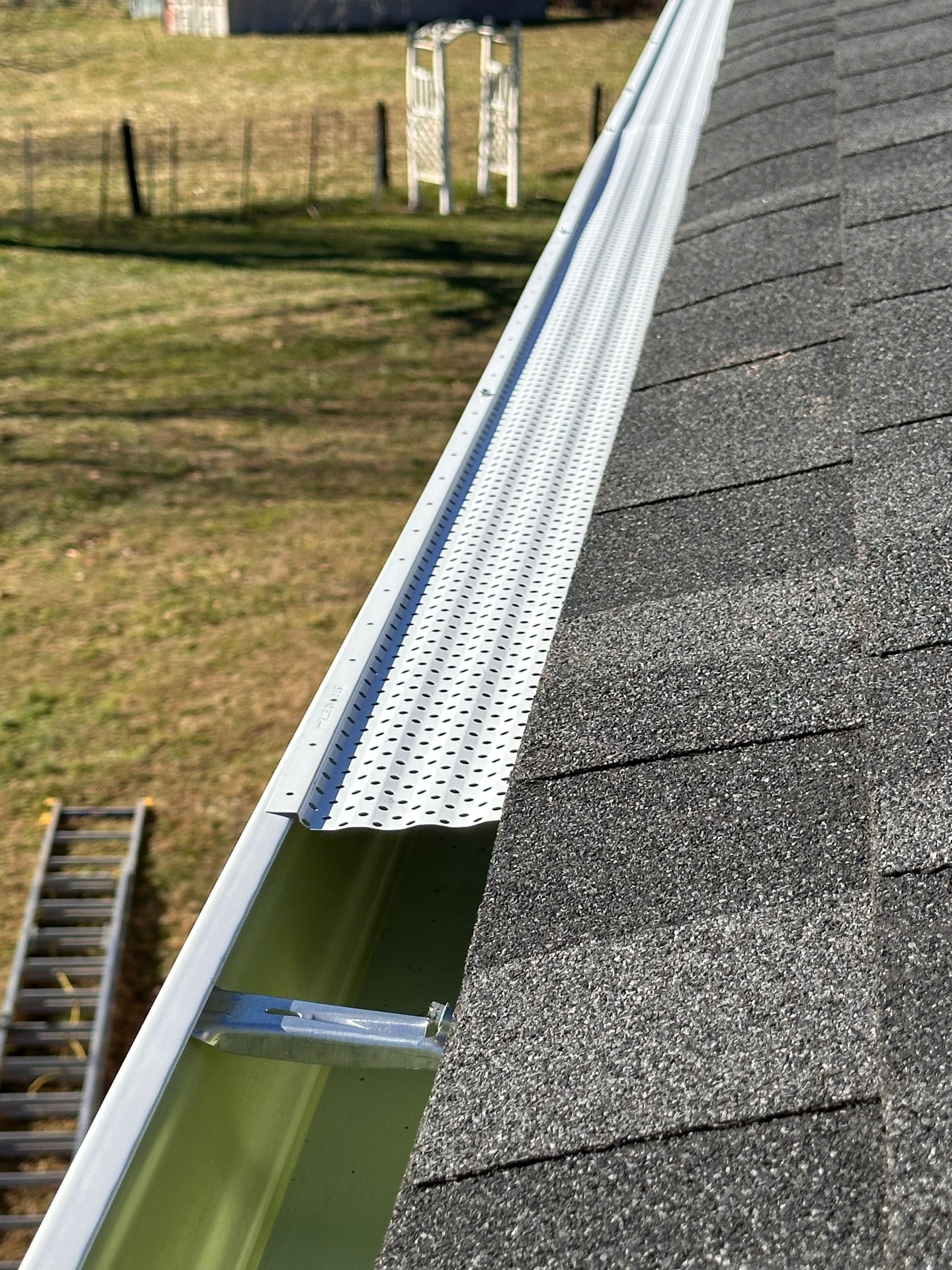 Man installing bird deterrent on a roof's edge, near a brick wall, with a skylight above.