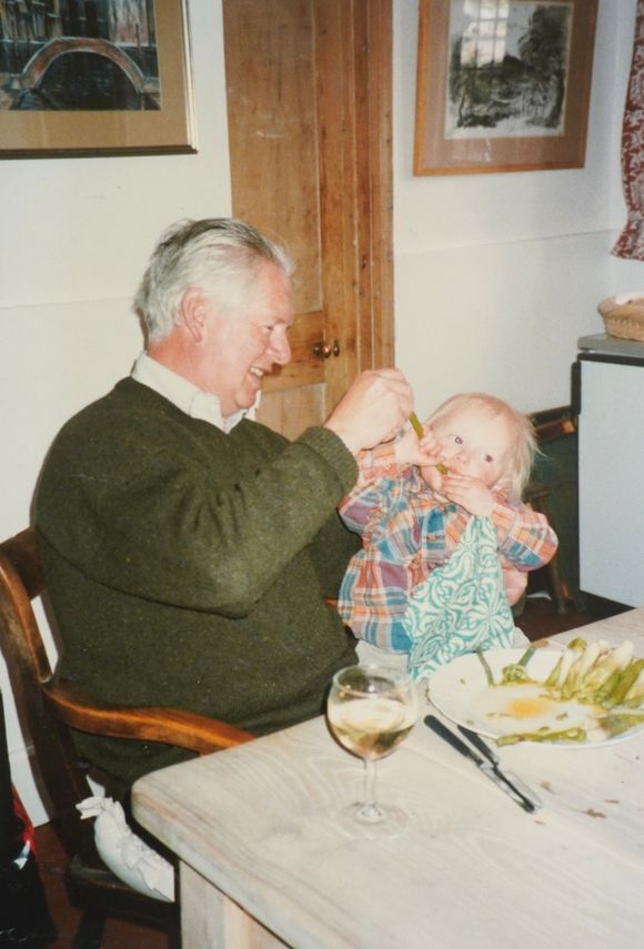 Elderly person feeding a child at a table. Child has food on face.