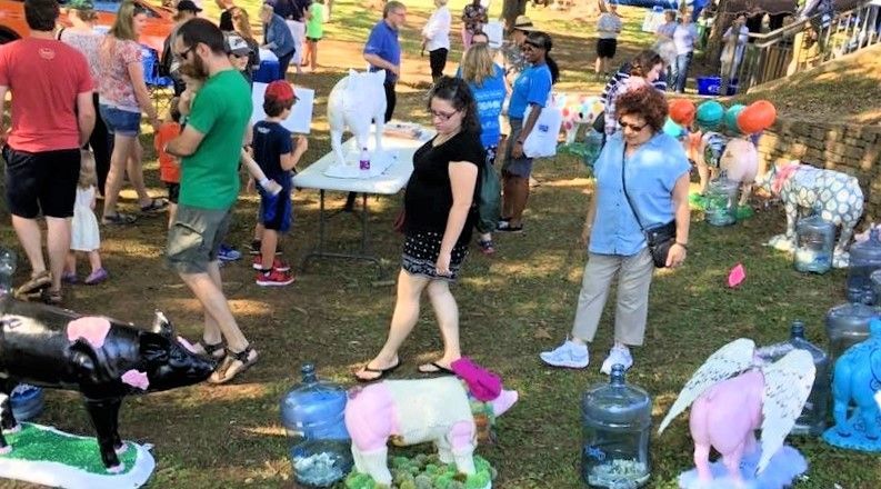 People walking through display of painted pig statues