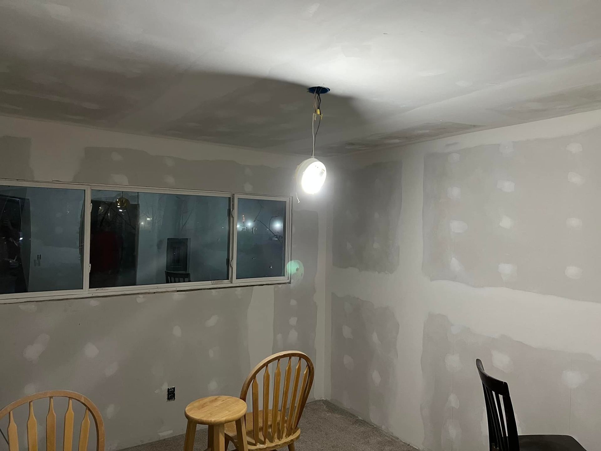 Room with drywall, a hanging light, a window, and two chairs.