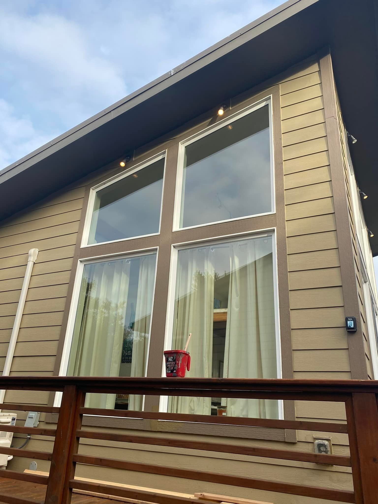 Exterior of a house with large windows, brown siding, and a wooden deck railing.