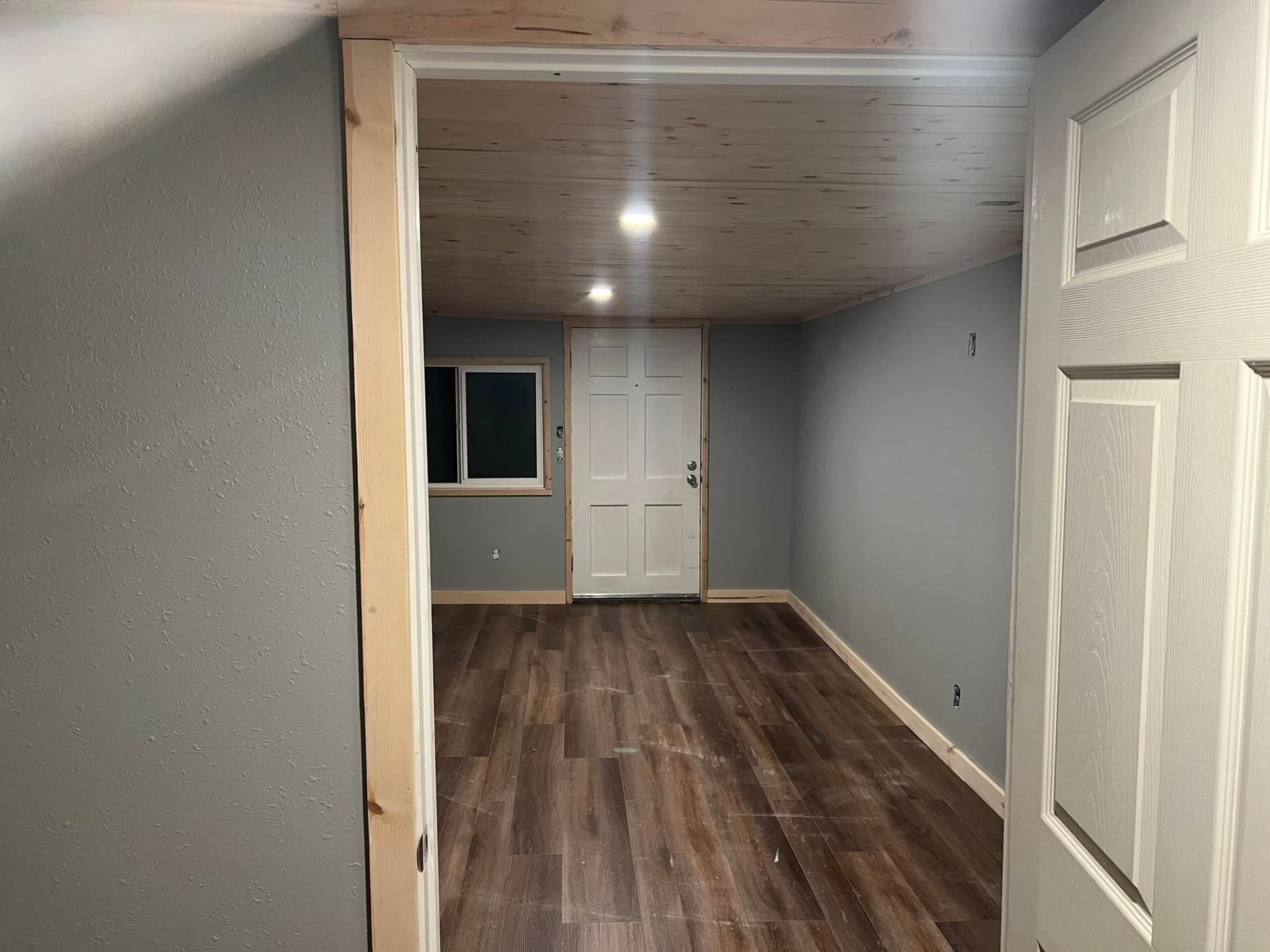 Interior room with gray walls, wood-look flooring, white door, and a window.
