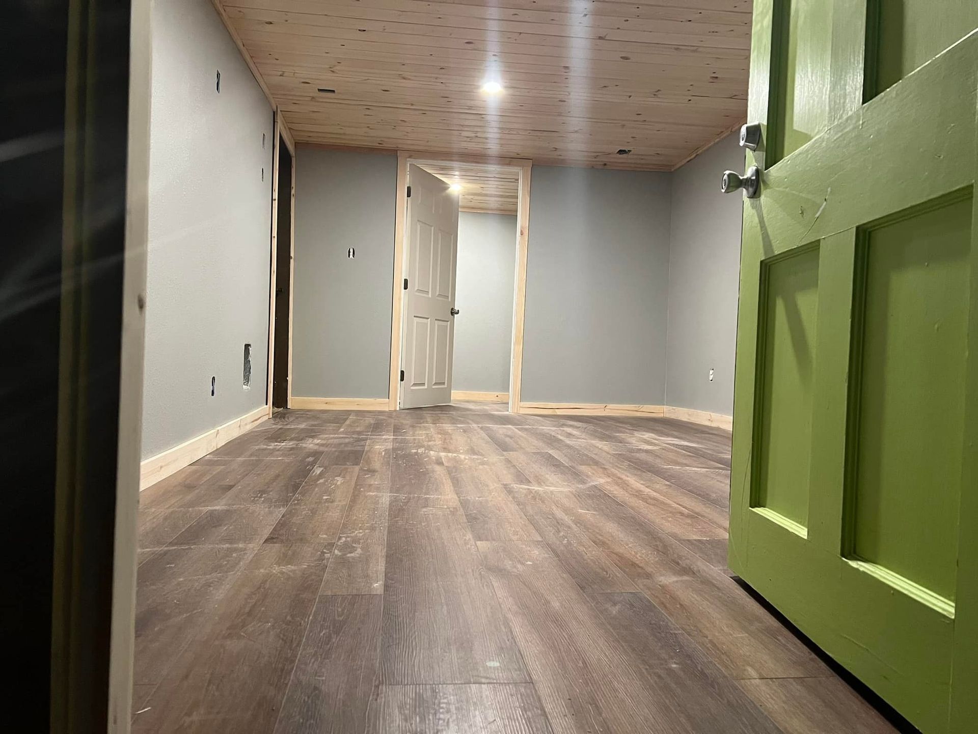 Interior view of a room with green door, wood floor, gray walls, and light wooden ceiling.