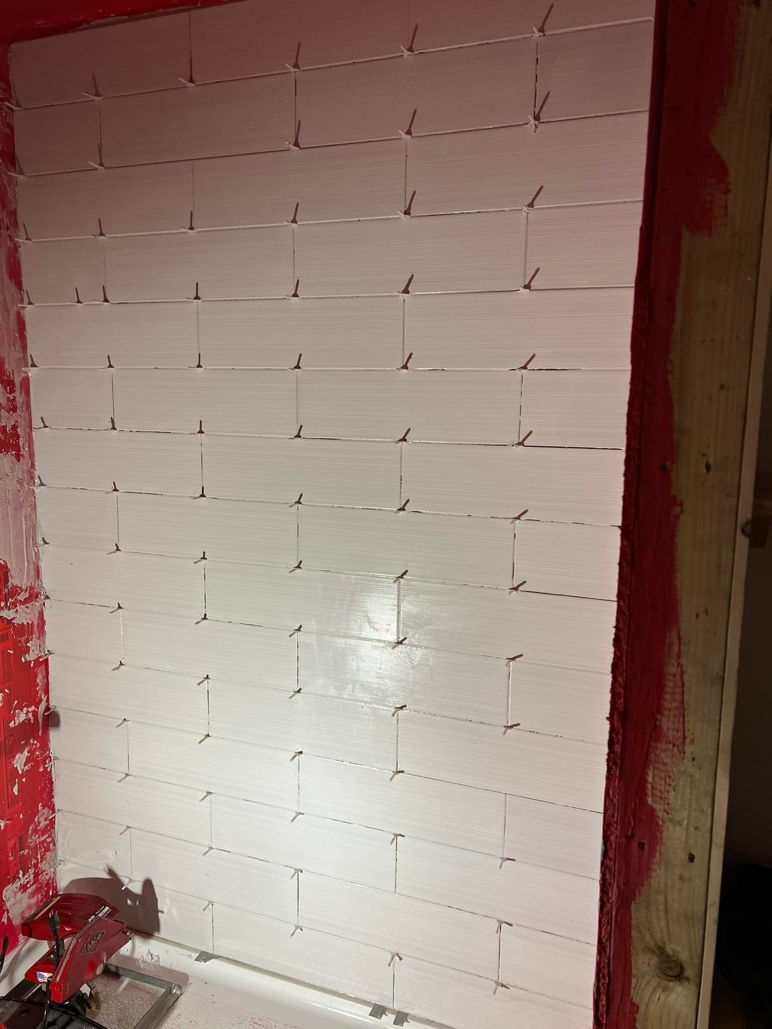 White subway tiles partially installed on a red-walled surface with tile spacers visible.