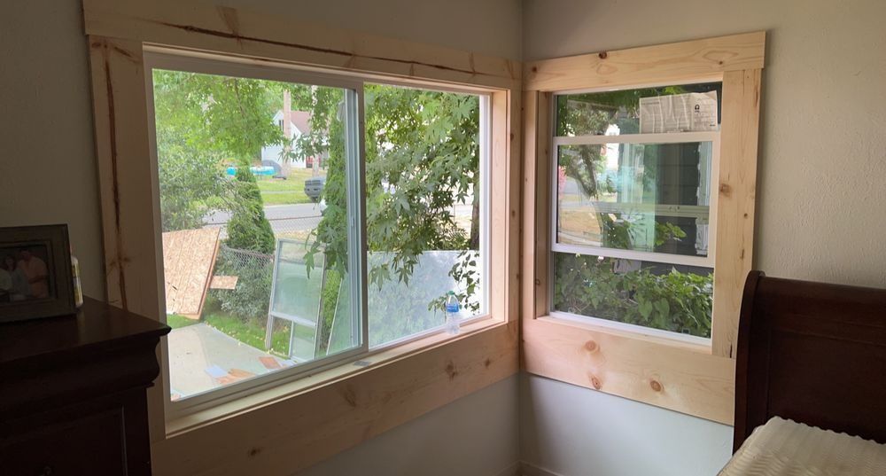Wooden window frames installed around two windows, with a view of trees and a street outside.