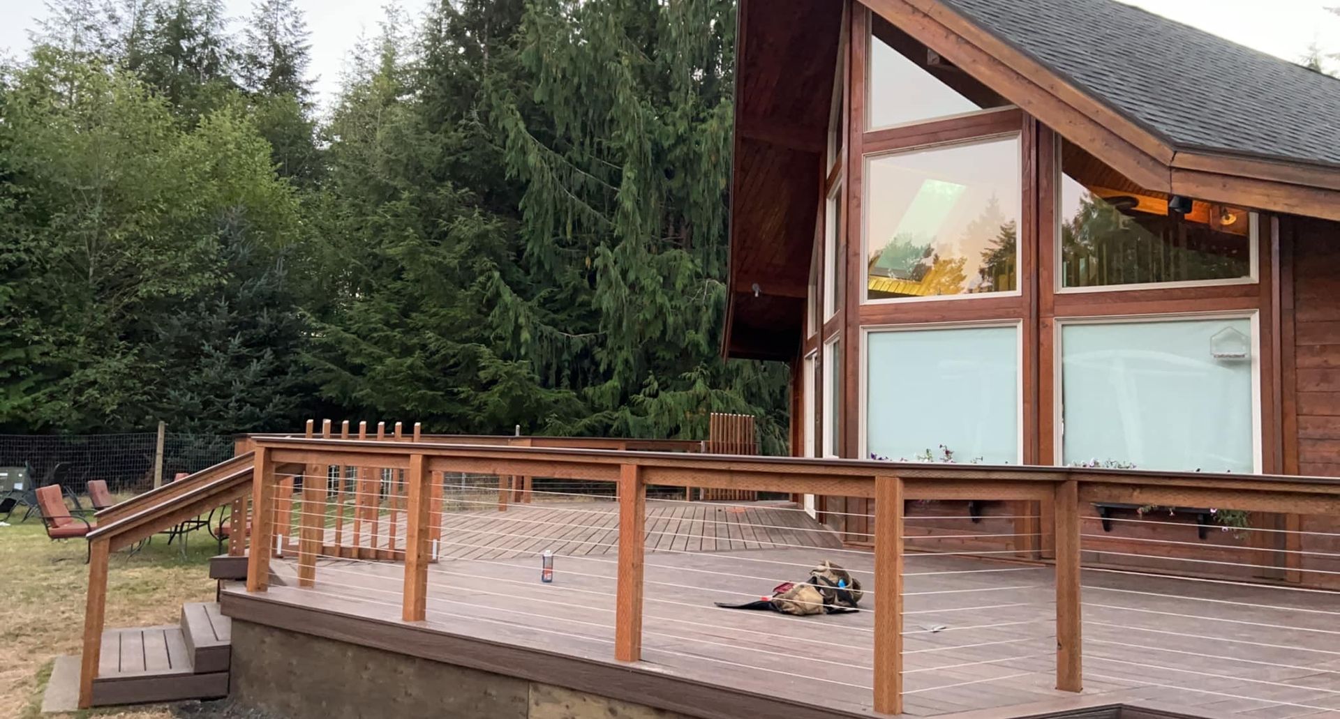 Wooden deck of a house with large windows, surrounded by trees.