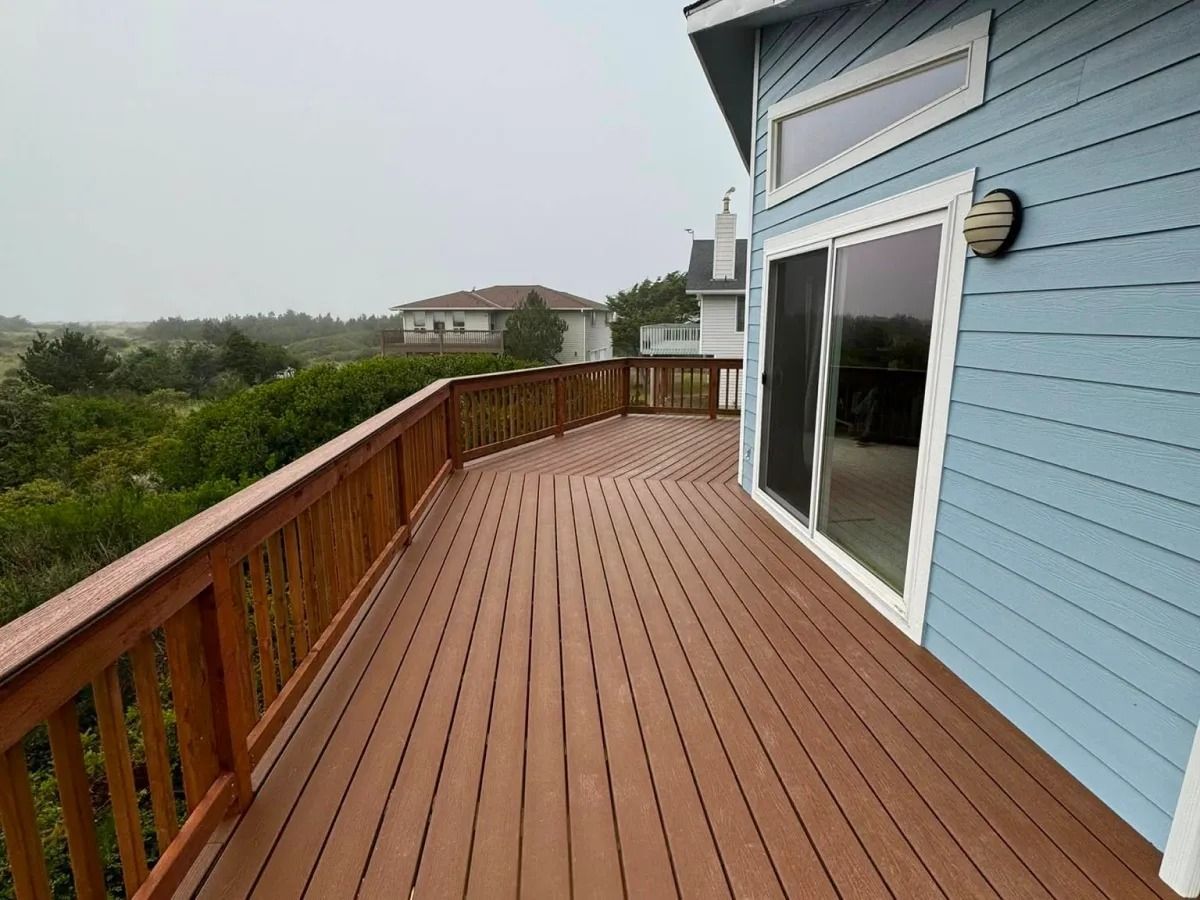 Wooden deck of a blue house overlooking a green landscape and other houses on an overcast day.