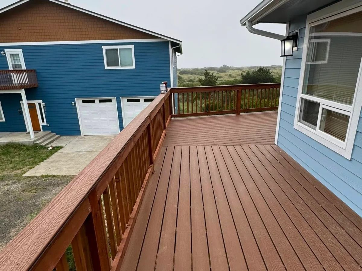 Wooden deck with brown railings next to a blue house with two white garage doors, overcast sky.