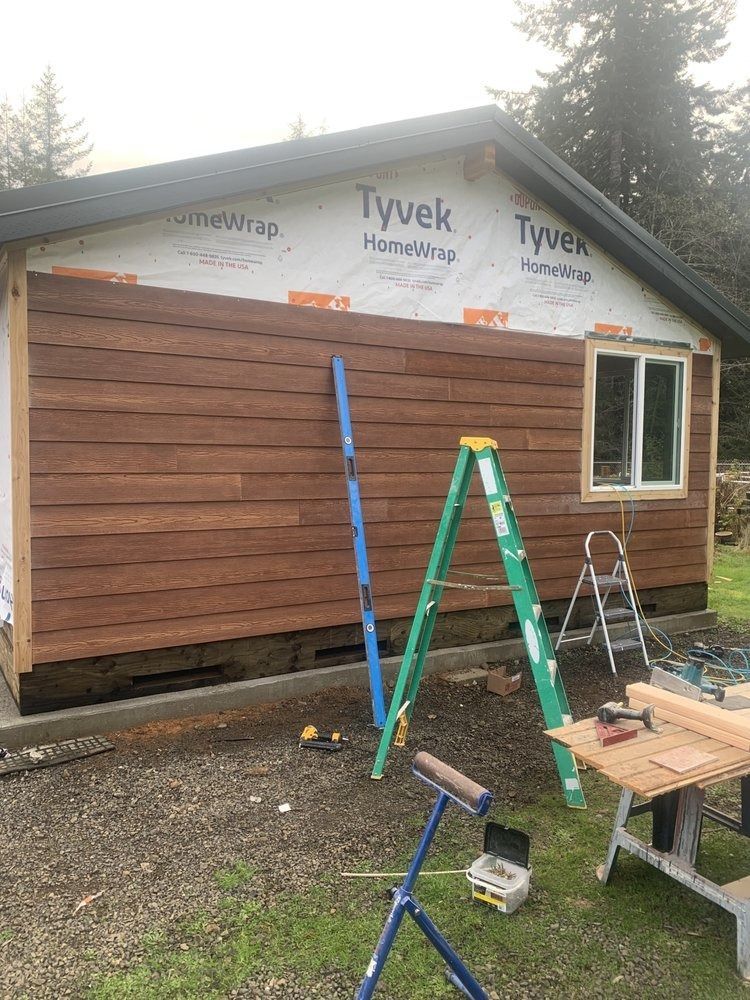 Exterior of a building under construction. Brown siding, green ladder, blue level, Tyvek wrap visible.
