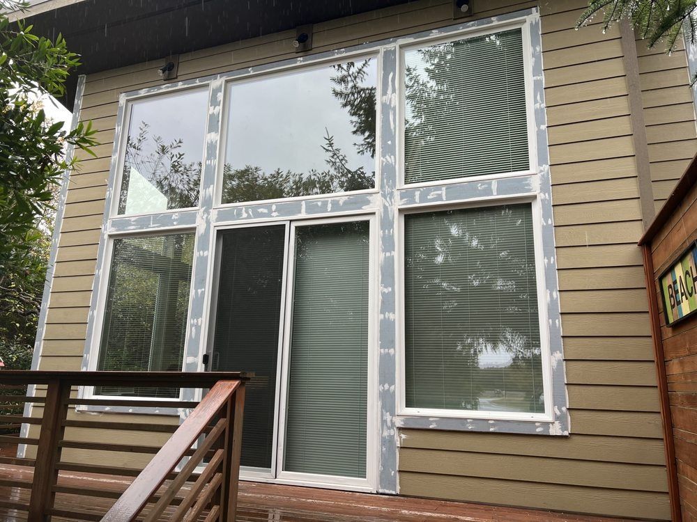 Exterior view of a building with large windows and sliding glass door; weathered gray trim.