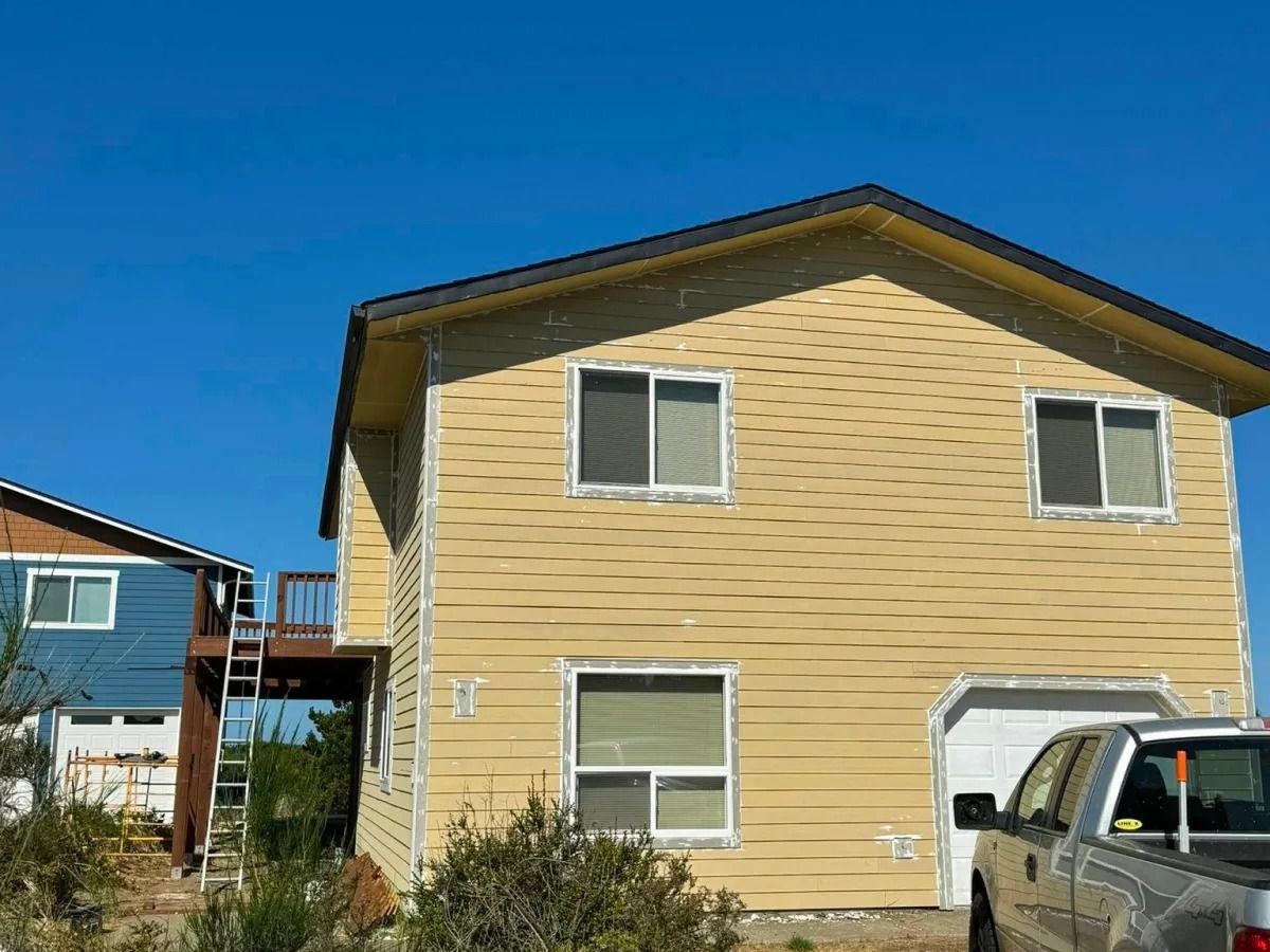 Two-story yellow house with a garage and a blue house next door under a clear blue sky.