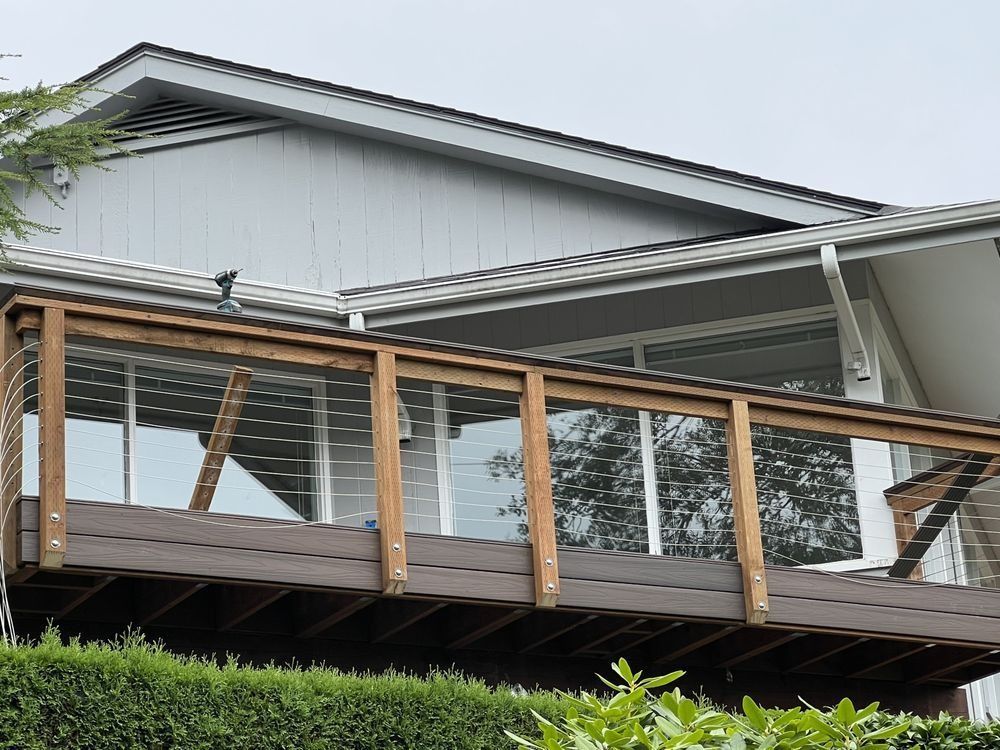 Wooden deck with glass railing attached to a two-story gray house.