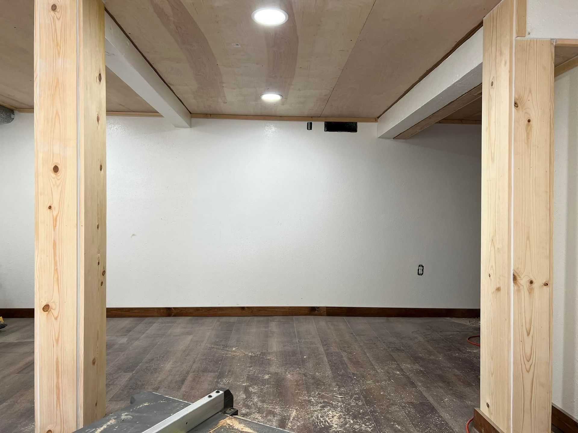Basement room with wooden posts, white walls, wood ceiling, and dark wood floor.
