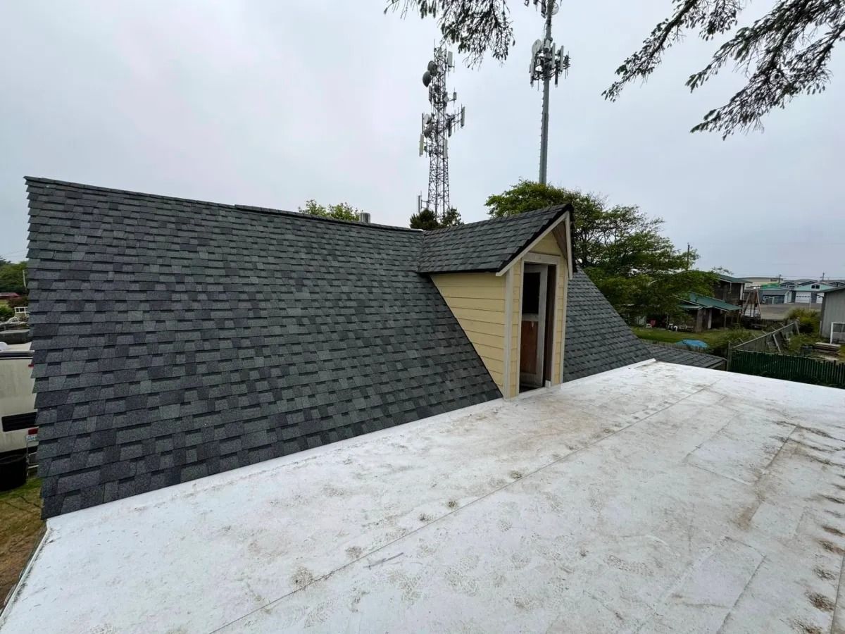 Grey shingled roof with a small, tan-colored structure; white flat roof in foreground, cloudy sky.