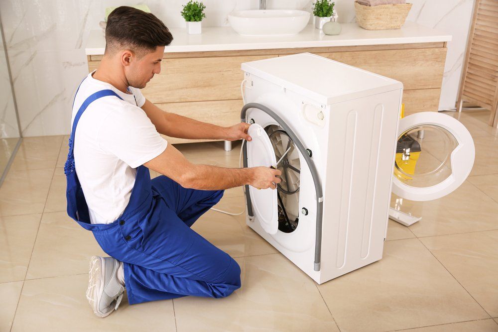 A Man is Fixing a Washing Machine in a Bathroom — Eurocoast Appliance Service In Tuggerah, NSW