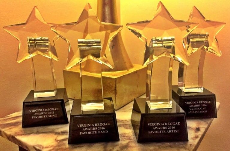 Four gold star-shaped trophies on a marble surface. Each has a rectangular base and engraved text, likely awards.