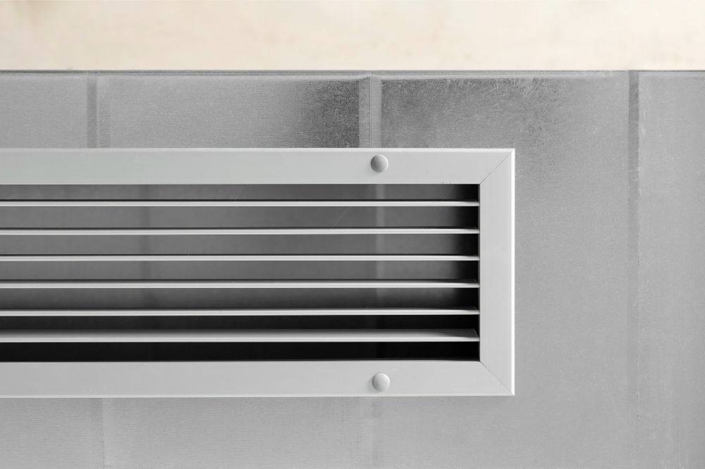 Inside of a rectangular air vent on a roof. Metal bars and walls are visible, lit by sunlight.