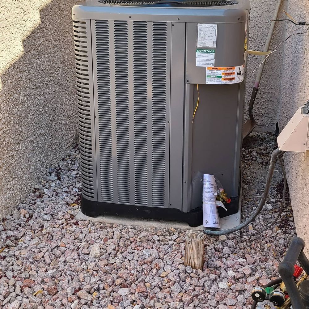 AC unit on a gravel base next to a stucco wall, with electrical conduit and a wooden post.