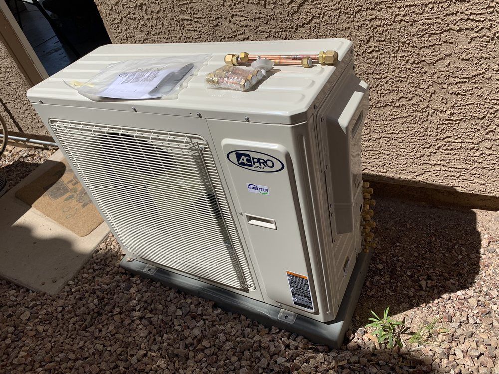 Outdoor heat pump unit on a gravel surface. A small instruction sheet and fittings sit on top.