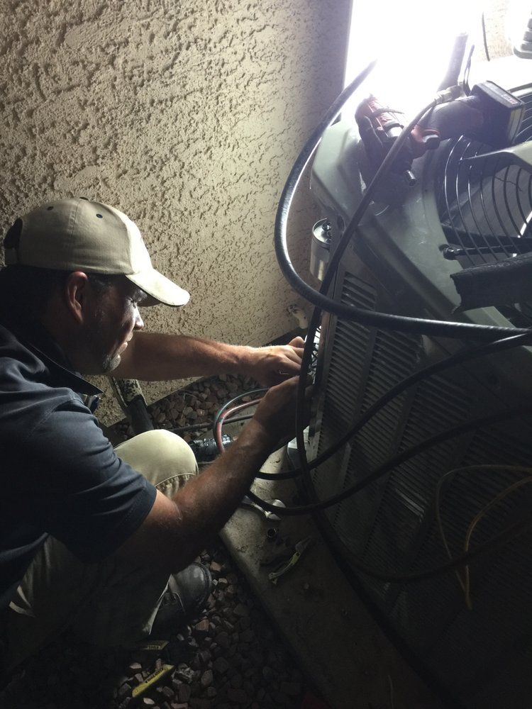 HVAC technician working on an outdoor air conditioning unit. Dark setting, wearing a hat, focused.