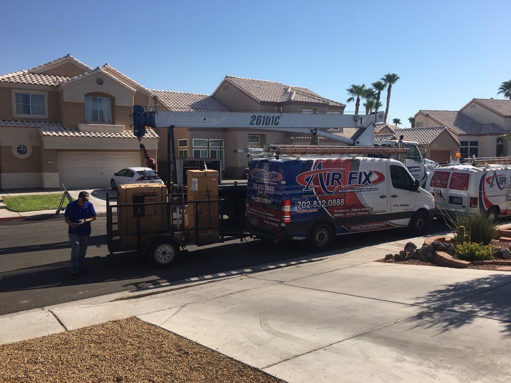 AC repair truck with crane parked in front of a house, boxes on a cart, worker in blue shirt.