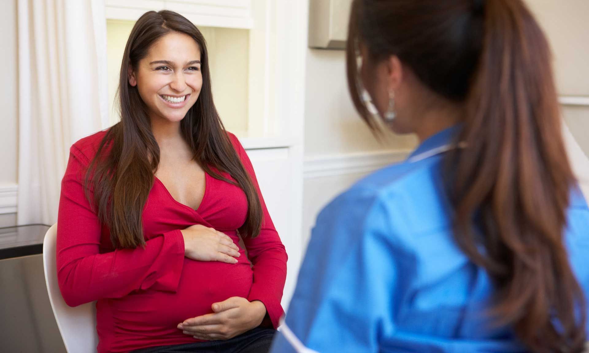 A pregnant woman holding her stomach in front of a nurse